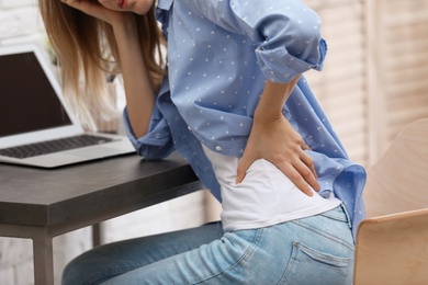 Young woman suffering from back pain in office, closeup