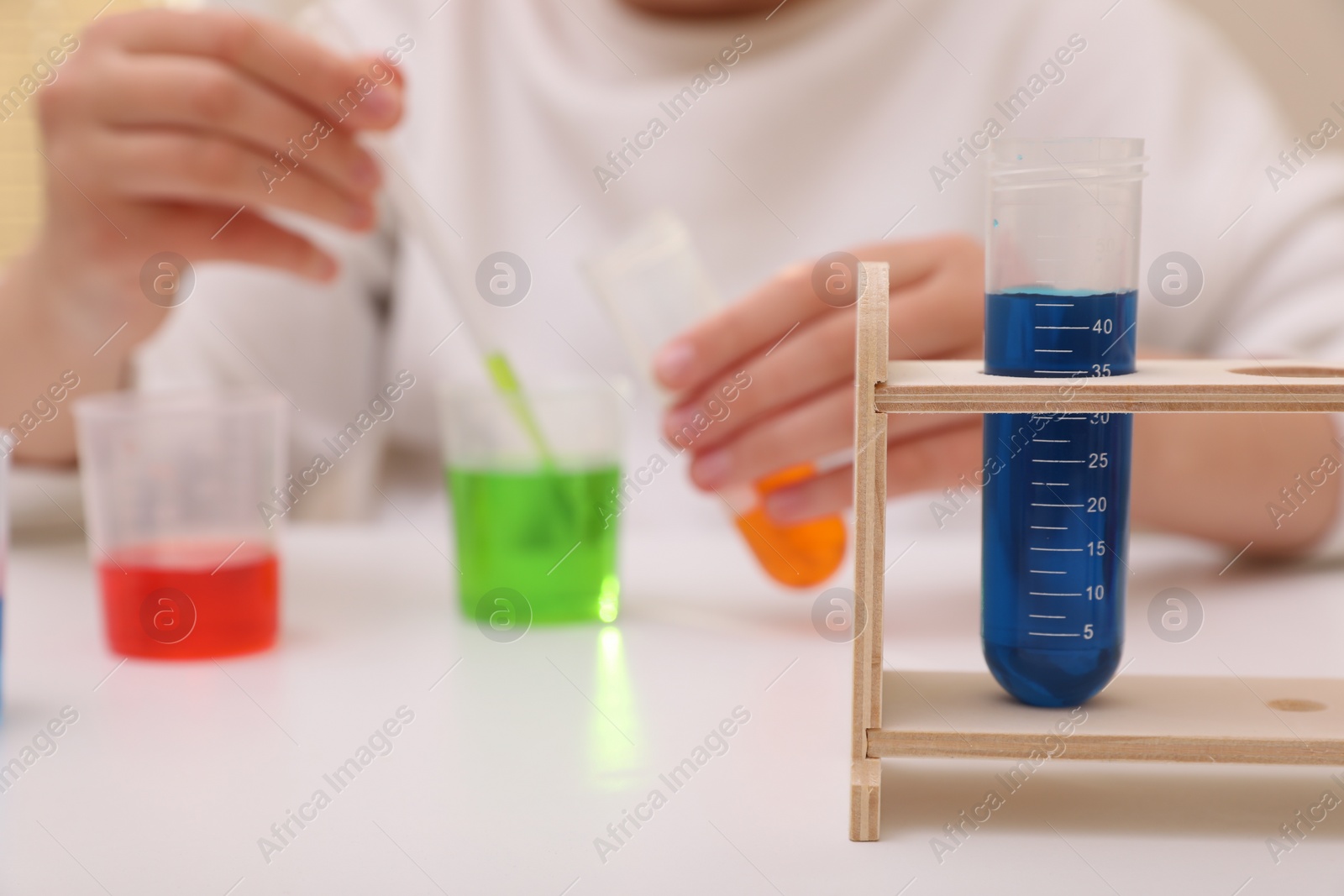 Photo of Girl mixing colorful liquids at white table indoors, selective focus. Kids chemical experiment set