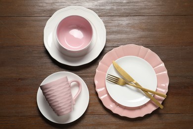 Beautiful ceramic dishware, cutlery and cup on wooden table, flat lay