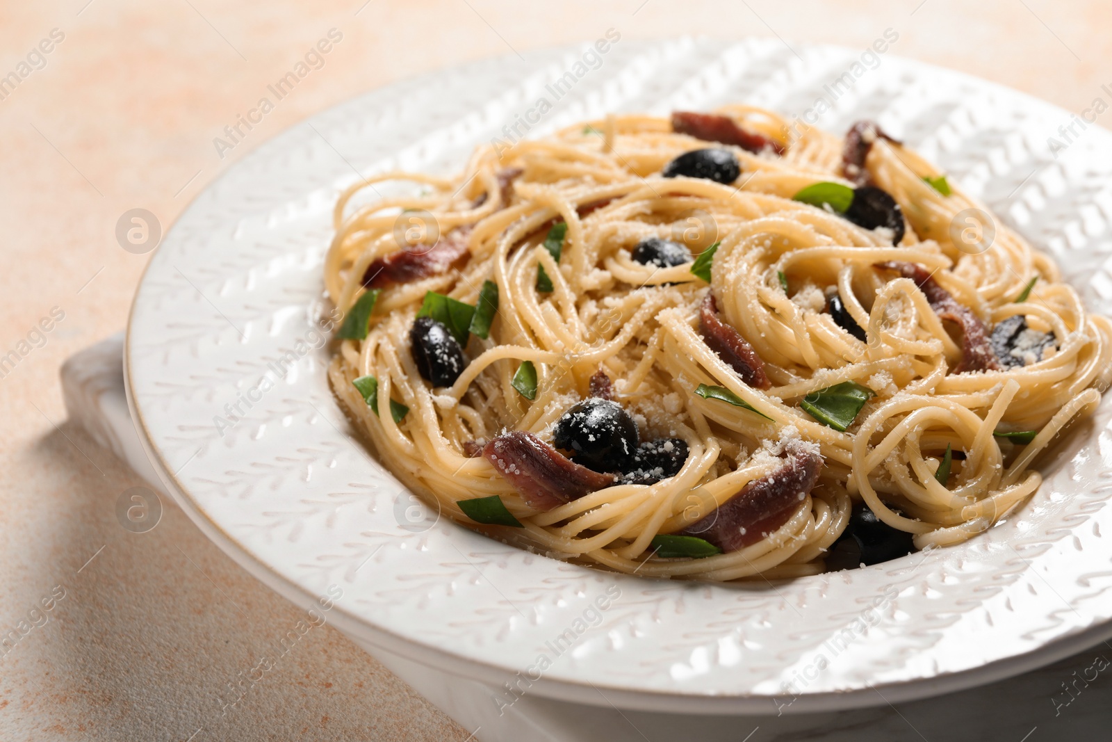 Photo of Delicious pasta with anchovies, olives and parmesan cheese on beige textured table, closeup