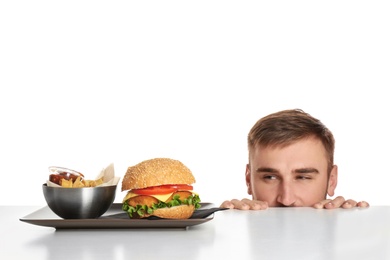 Young man and plate with French fries and tasty burger on white background