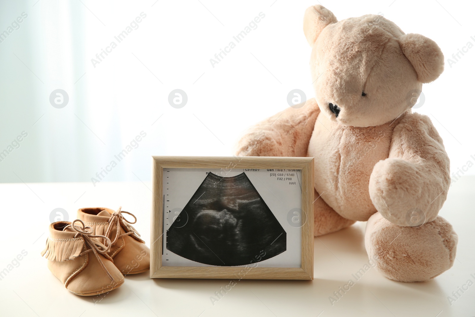 Photo of Ultrasound picture, teddy bear and baby shoes on table against light background. Space for text