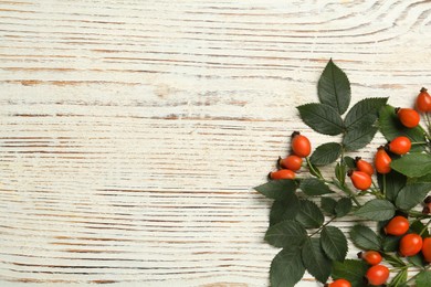 Ripe rose hip berries with green leaves on white wooden table, flat lay. Space for text