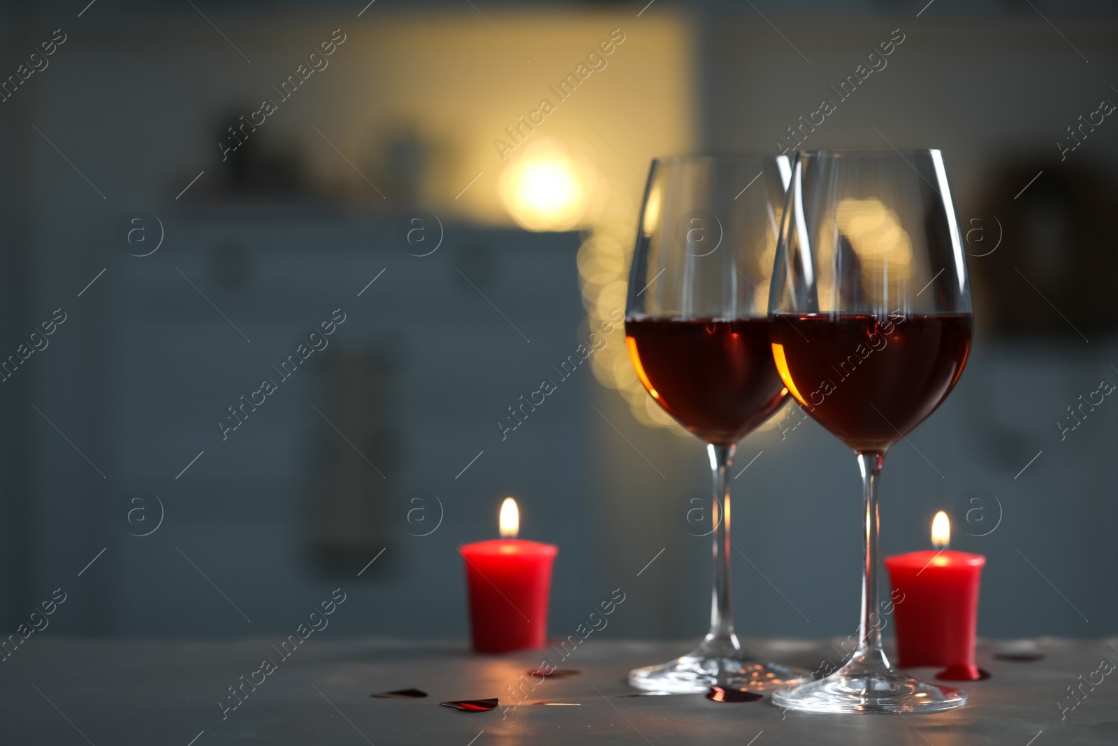 Photo of Glasses of red wine and burning candles on grey table against blurred lights, space for text. Romantic atmosphere