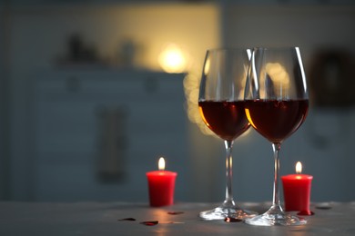 Glasses of red wine and burning candles on grey table against blurred lights, space for text. Romantic atmosphere