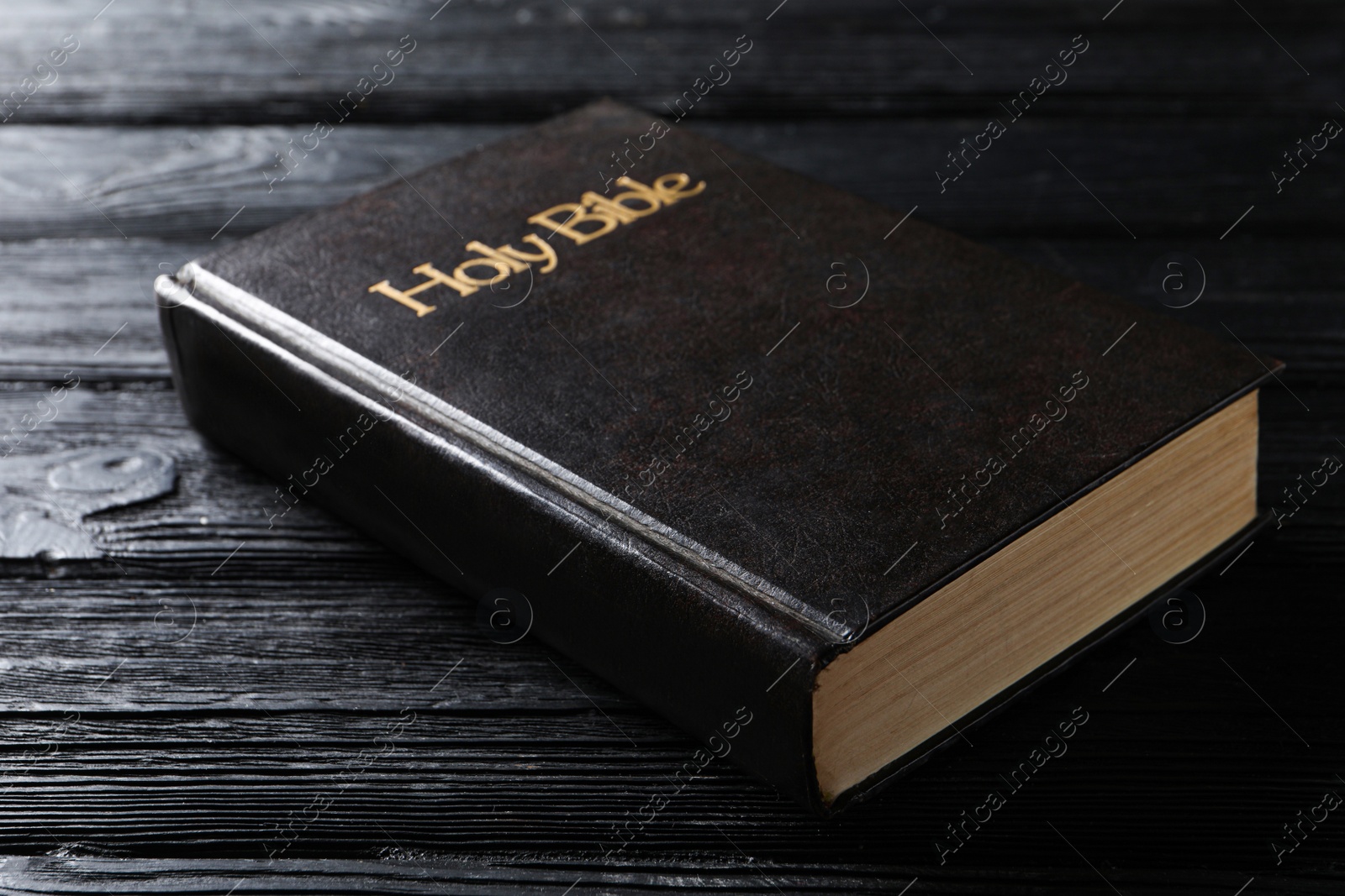 Photo of Bible with dark cover on black wooden table. Christian religious book