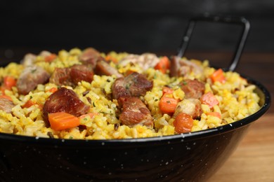 Photo of Delicious pilaf with meat and carrot on wooden table, closeup