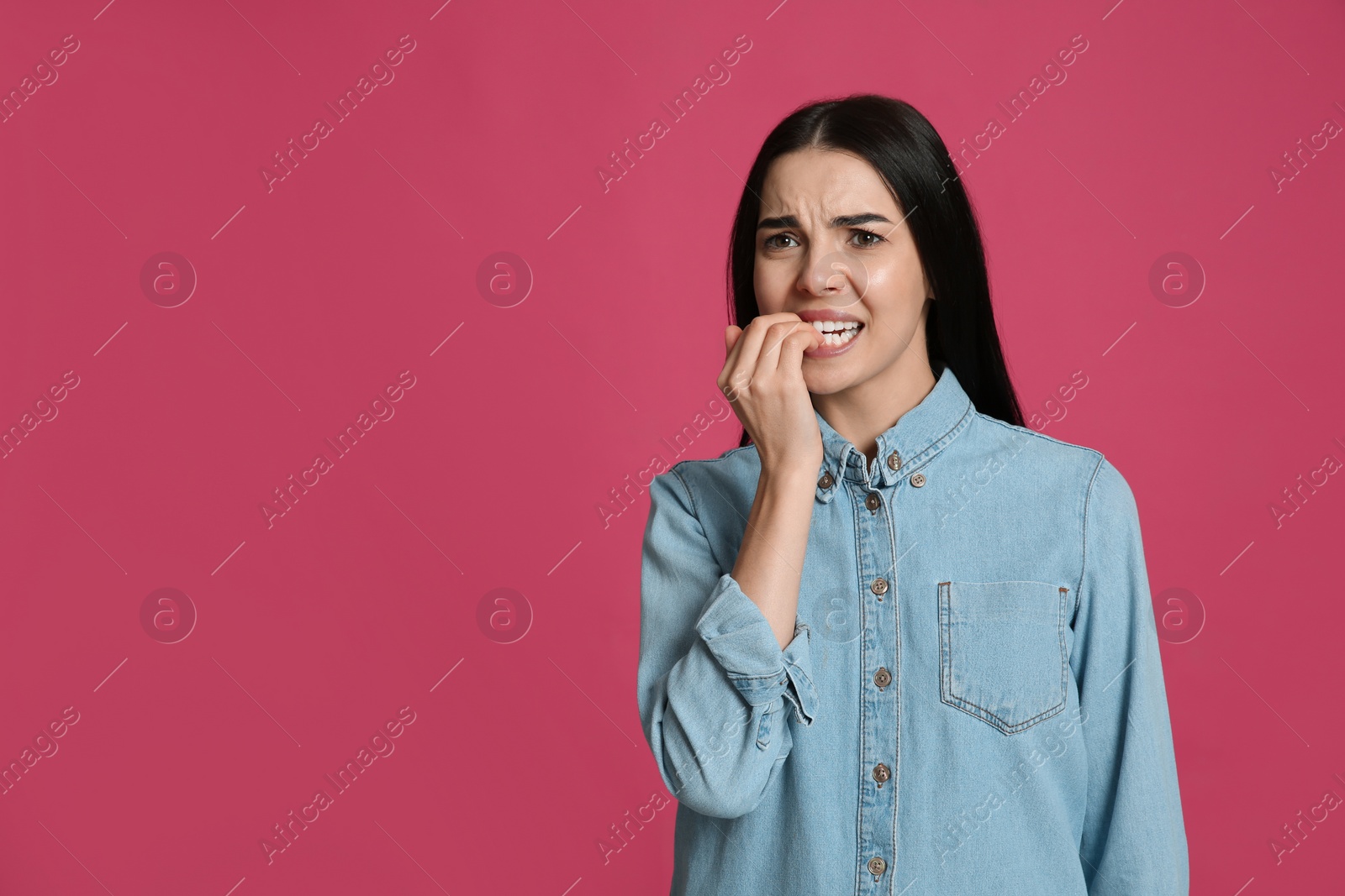 Photo of Young woman biting her nails on pink background. Space for text