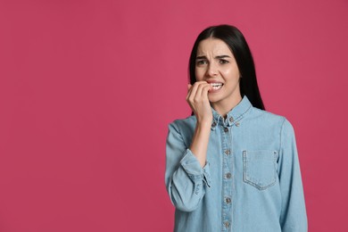 Young woman biting her nails on pink background. Space for text