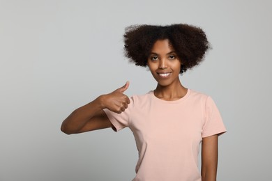 Photo of Smiling African American woman showing thumbs up on light grey background. Space for text