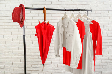 Rack with stylish clothes near white brick wall