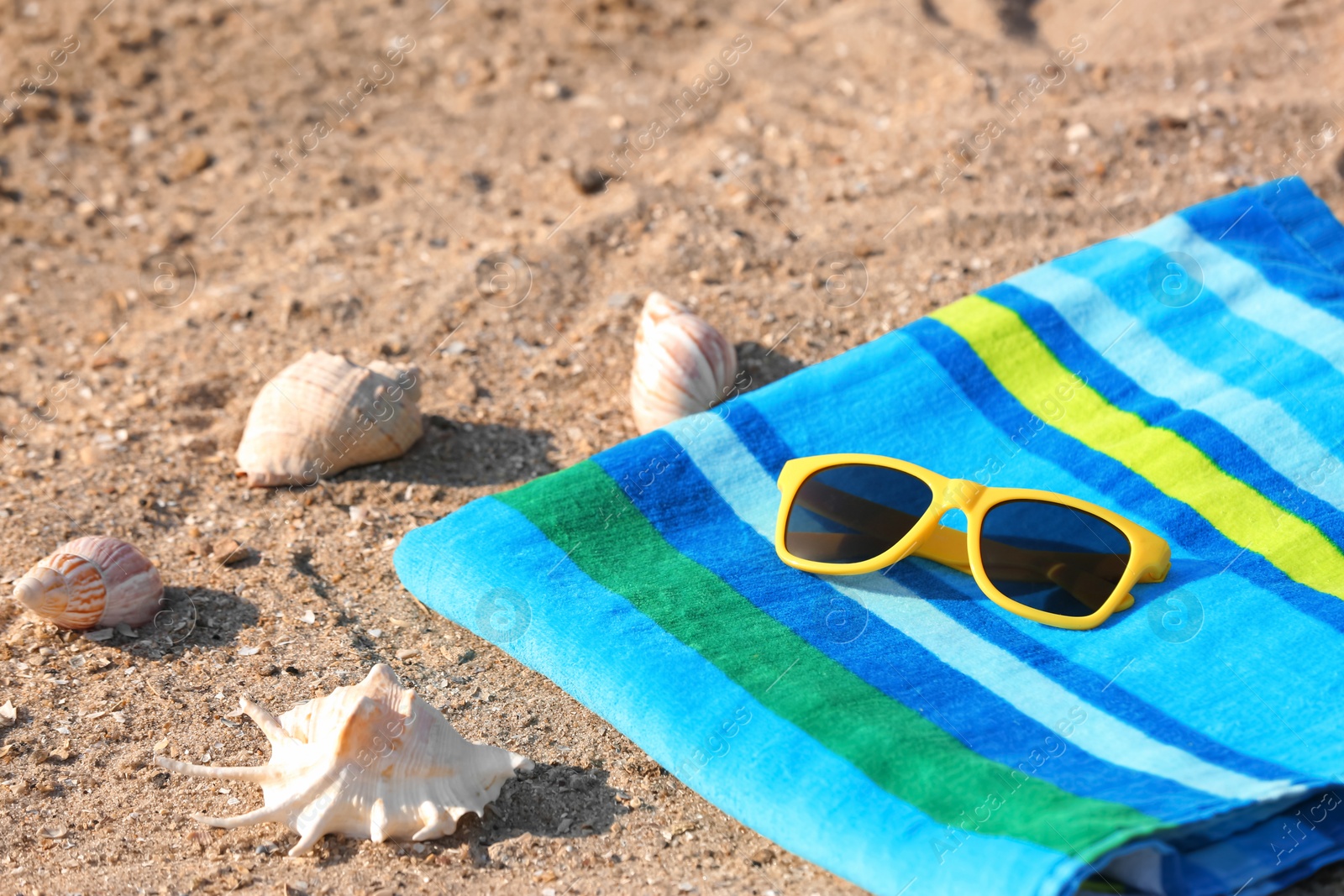 Photo of Bright towel and sunglasses on sand. Beach object