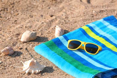 Photo of Bright towel and sunglasses on sand. Beach object