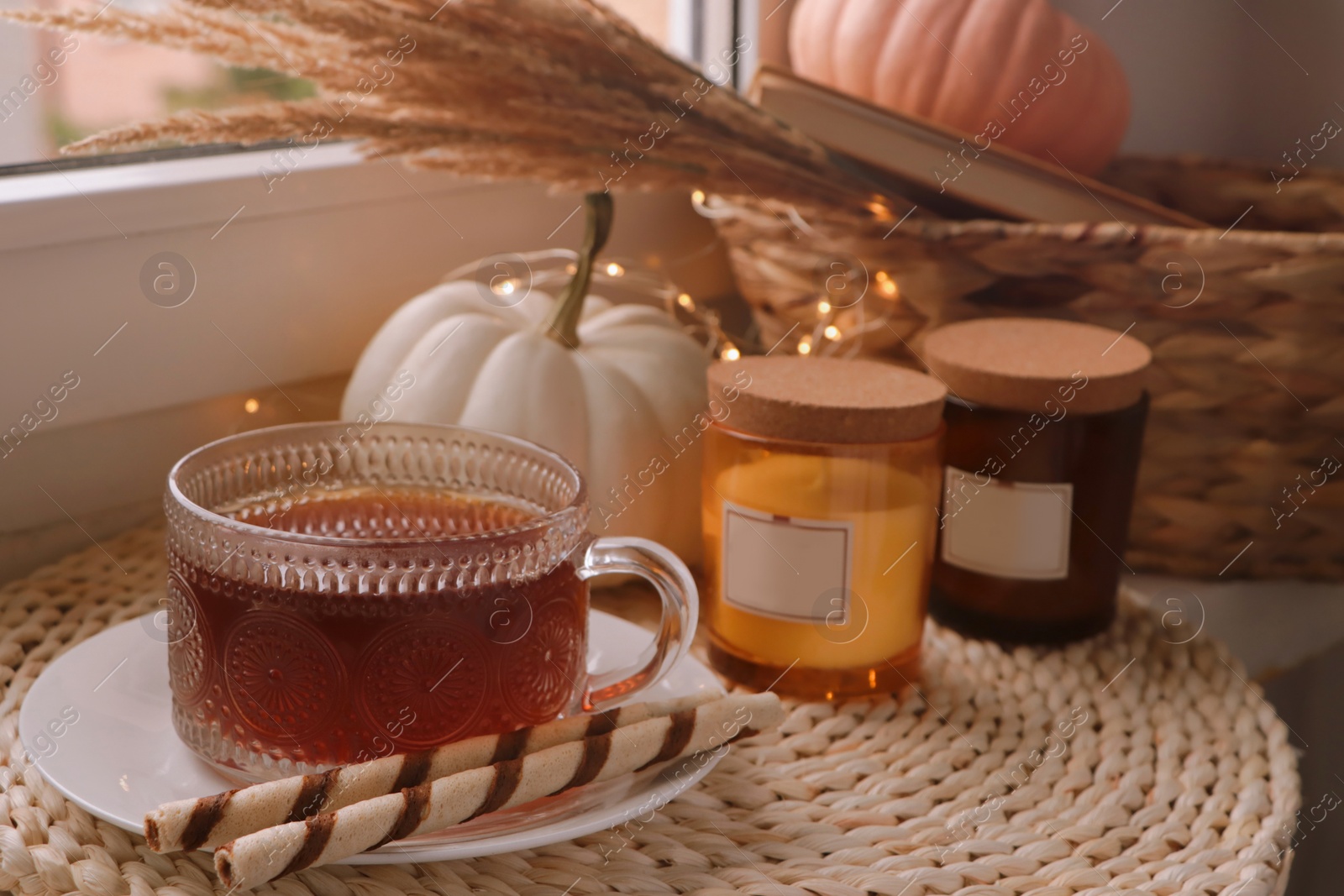 Photo of Cup of hot drink, cookies, candles and pumpkins on window sill indoors