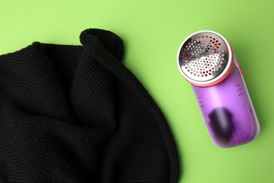 Photo of Modern fabric shaver and sweater with lint on light green background, flat lay