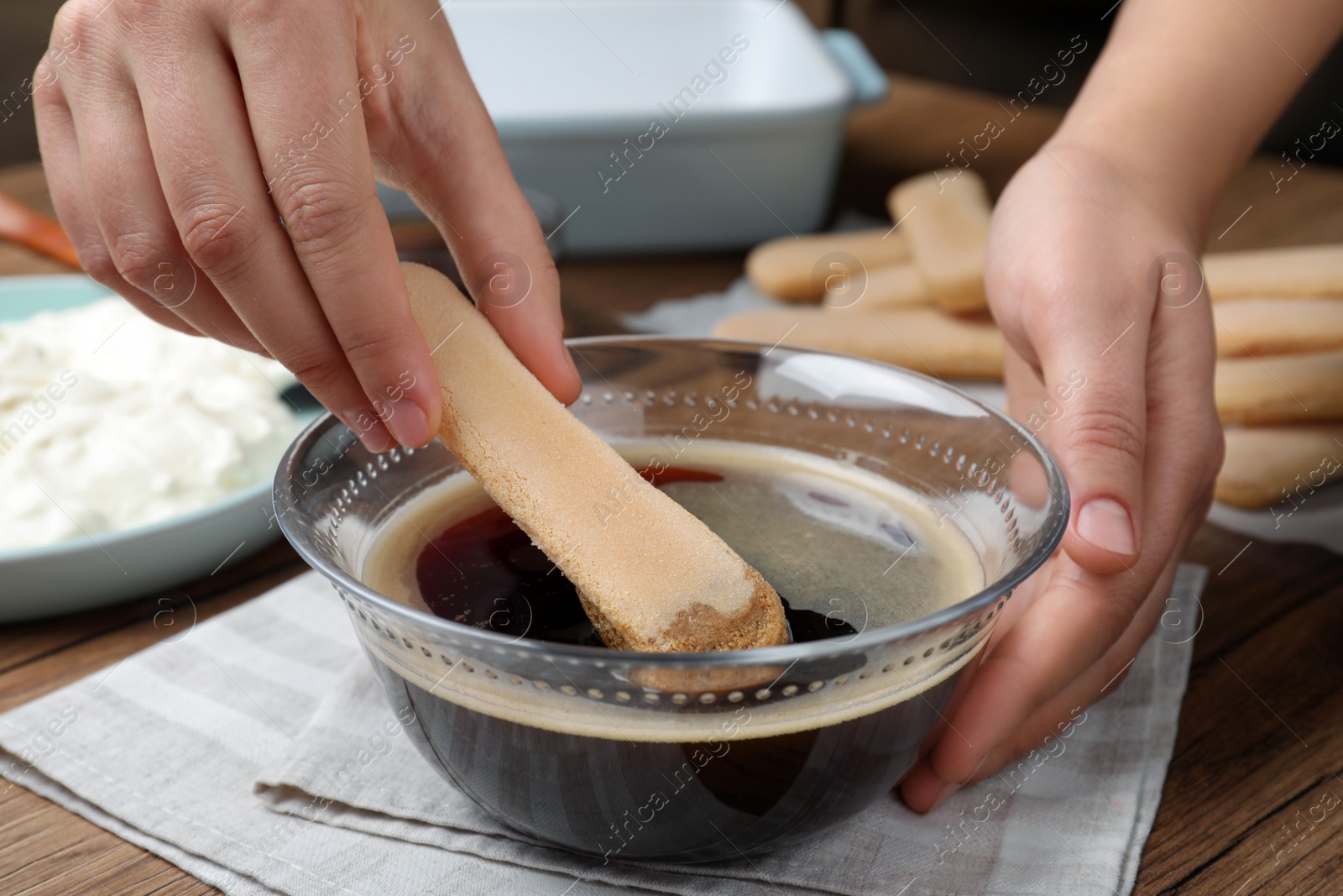 Photo of Woman making tiramisu cake at wooden table, closeup