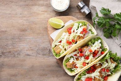 Yummy fish tacos served on wooden table, flat lay. Space for text