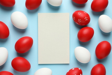 Flat lay composition of red painted Easter eggs and card on color background, space for text