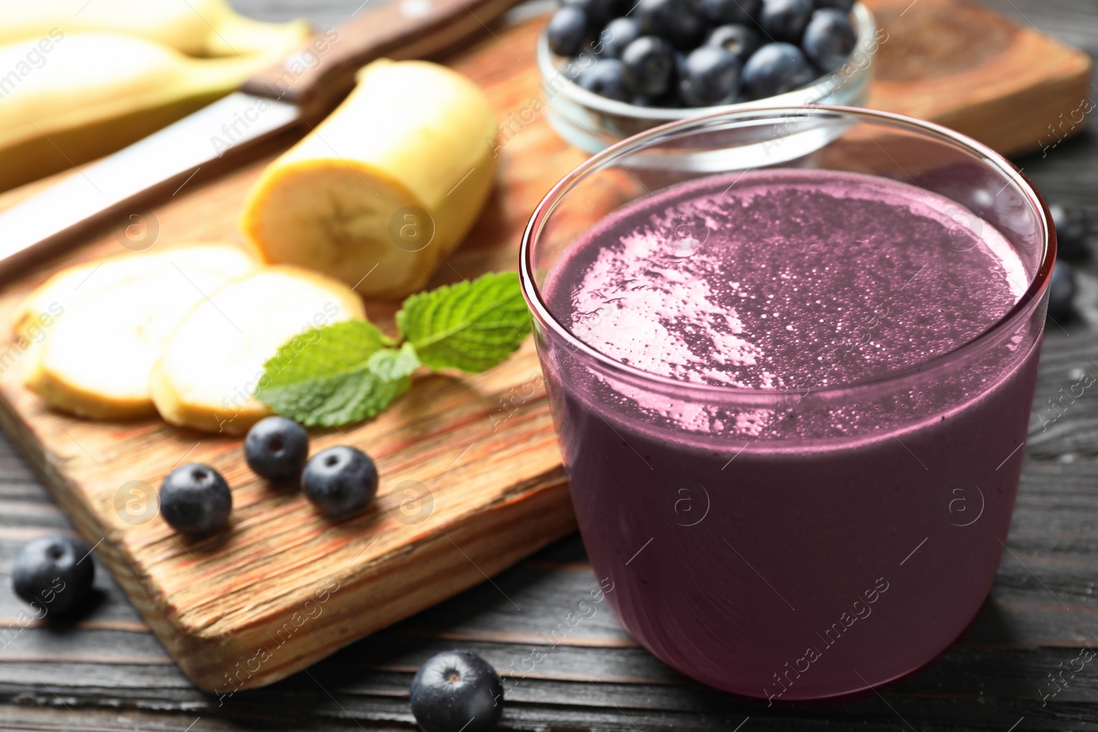 Photo of Fresh acai drink with banana and berries on dark wooden table, closeup