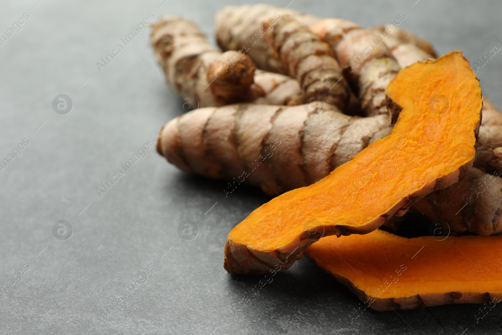 Photo of Whole and cut turmeric roots on grey table, closeup. Space for text