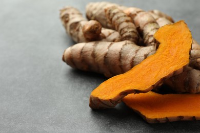 Whole and cut turmeric roots on grey table, closeup. Space for text