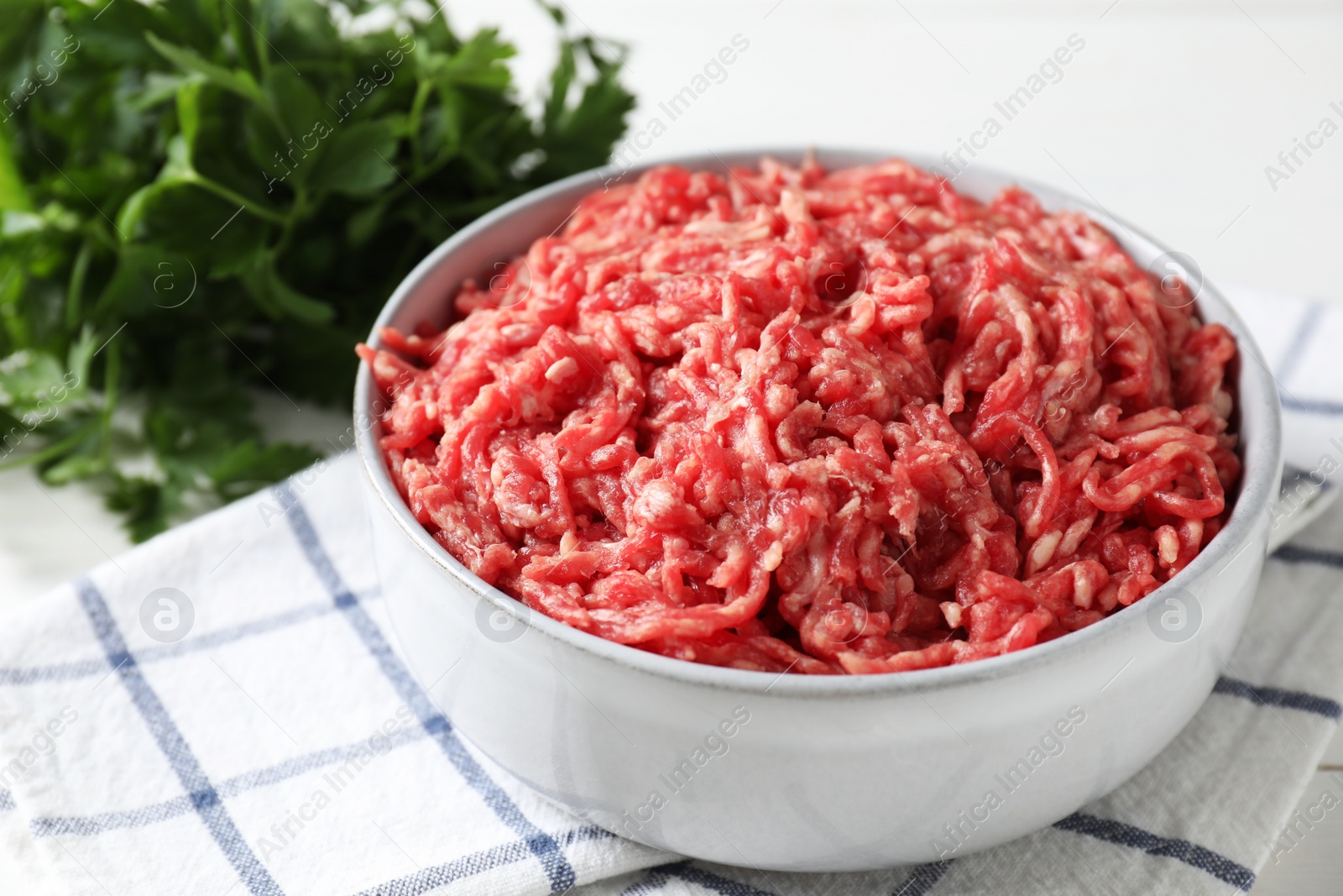 Photo of Raw ground meat in bowl and parsley on table, closeup