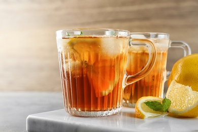 Photo of Cups of refreshing iced tea on table against wooden background