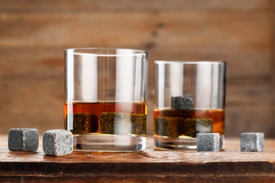 Photo of Whiskey stones and drink in glasses on wooden table, closeup