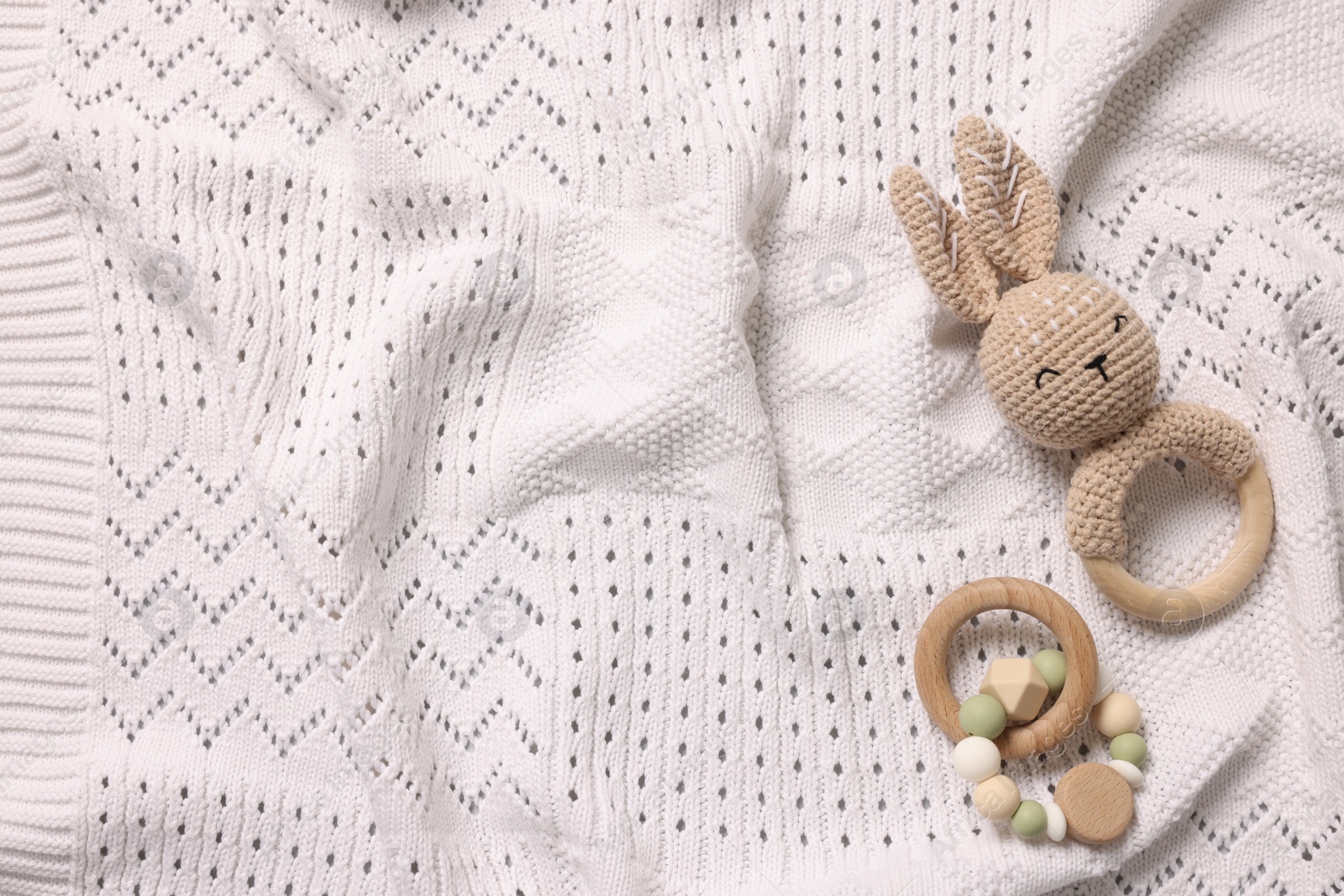 Photo of Baby accessories. Rattle and teether on white knitted fabric, top view. Space for text