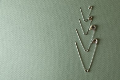 Photo of Many safety pins on green background, flat lay. Space for text