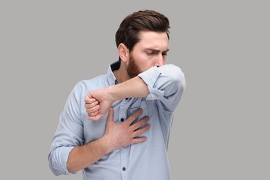 Photo of Sick man coughing into his elbow on light grey background, space for text. Cold symptoms