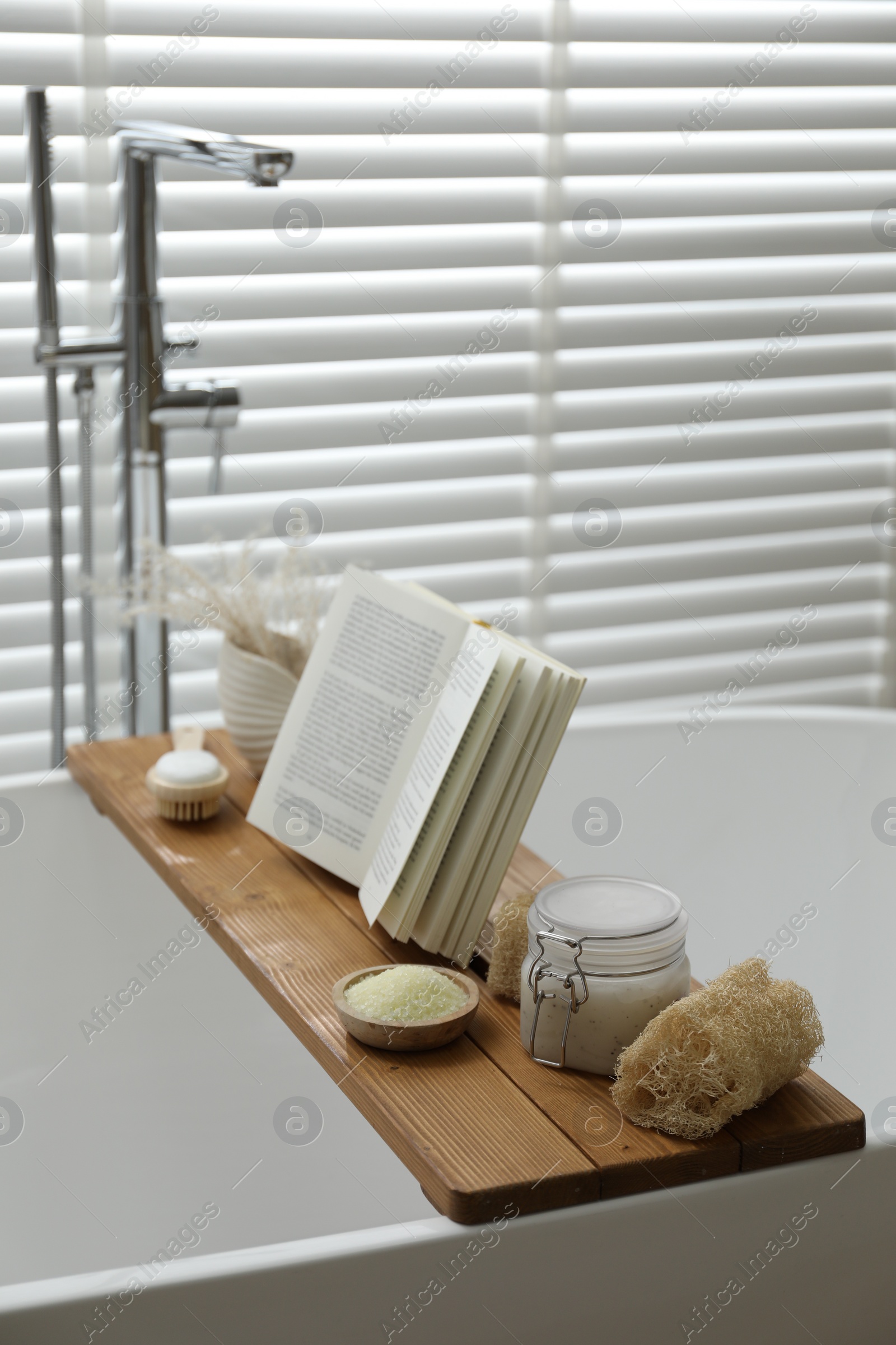 Photo of Wooden tray with spa products and book on bath tub in bathroom