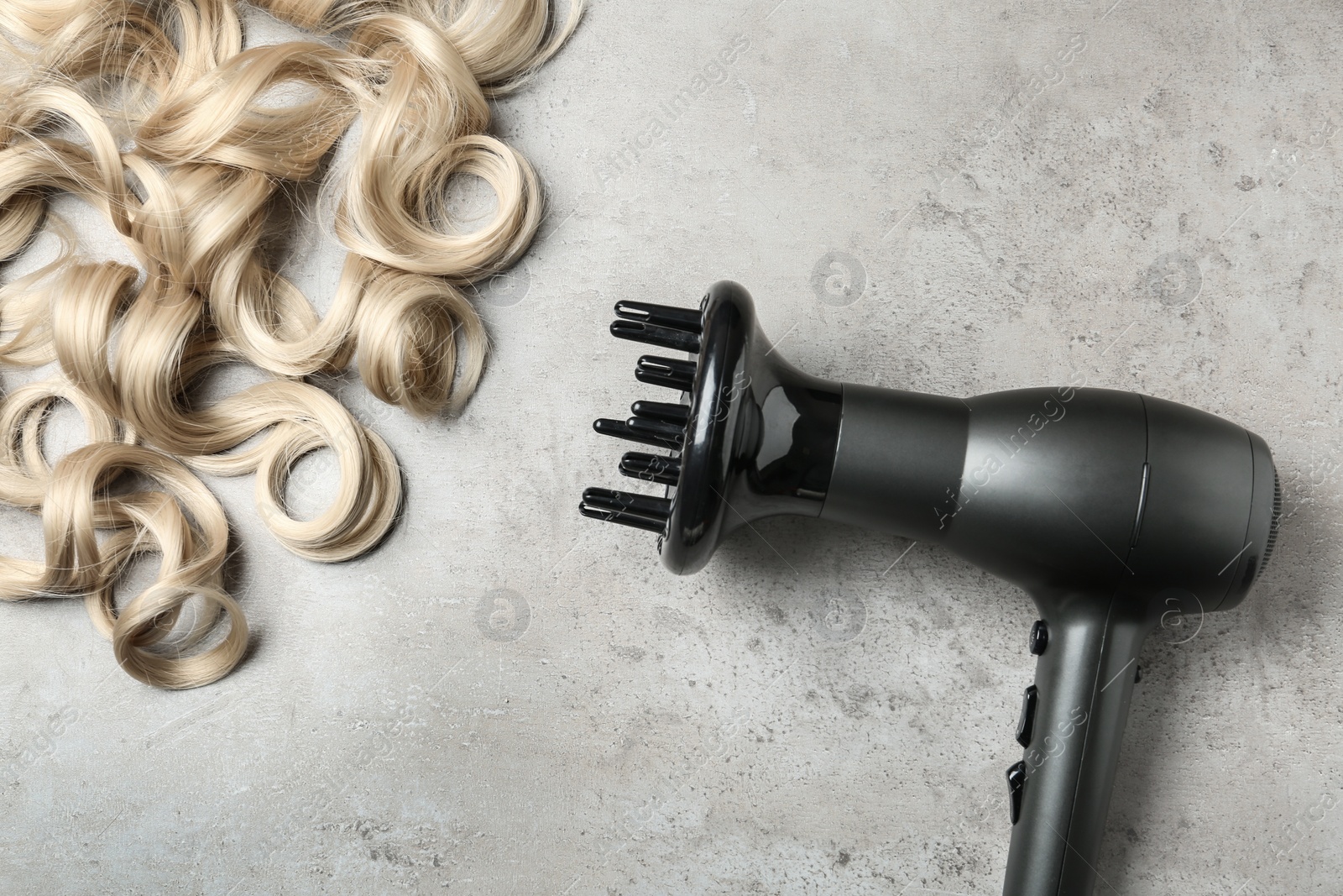 Photo of Curly hair locks and dryer on grey background, top view