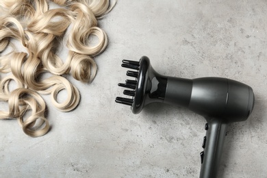 Curly hair locks and dryer on grey background, top view