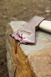 Axe with blood on stone outdoors, closeup