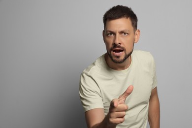 Aggressive man pointing on grey background, space for text