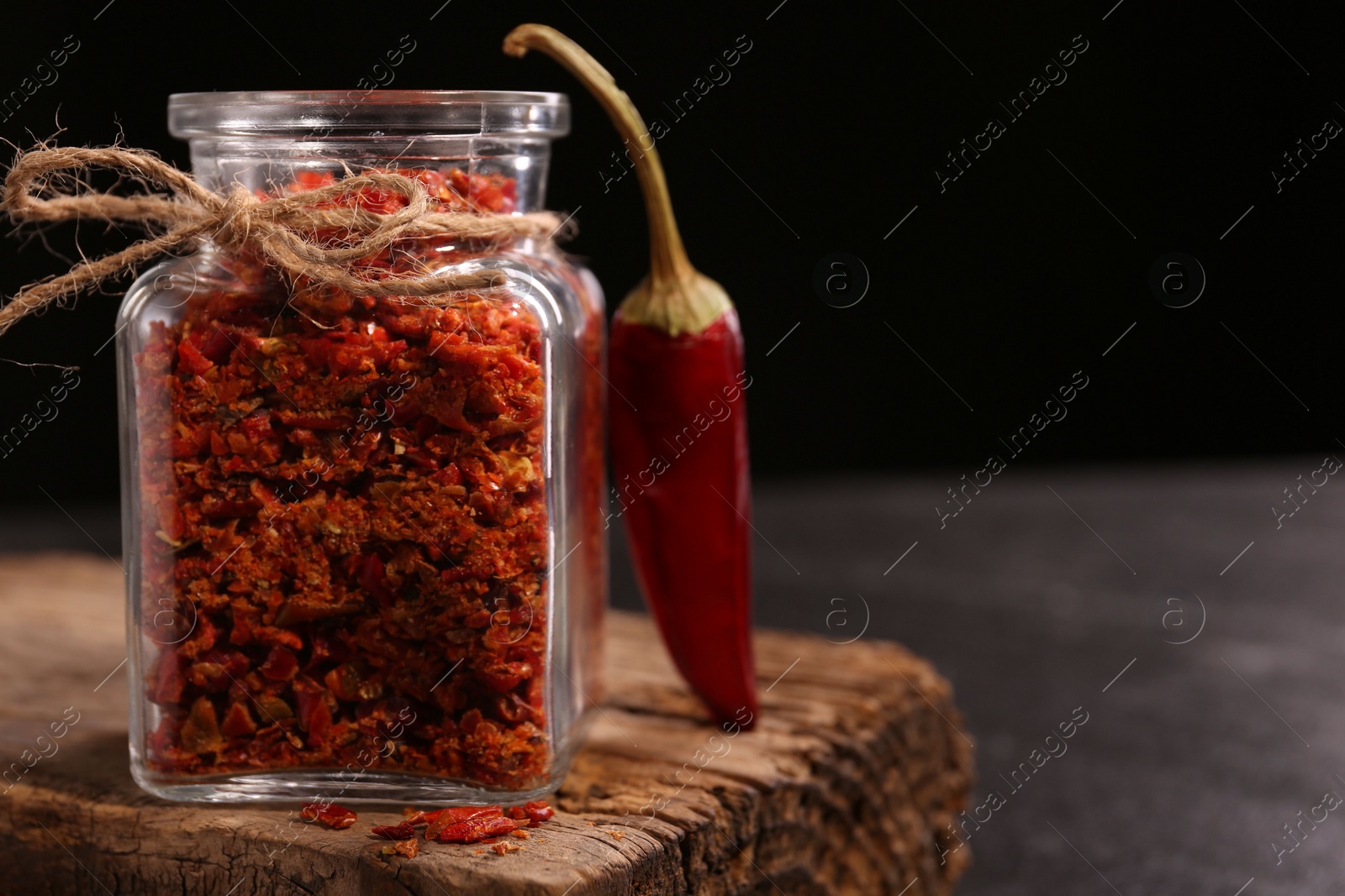 Photo of Chili pepper flakes in jar and pod on table against black background, closeup