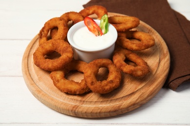 Photo of Wooden board with tasty onion rings and sauce on table