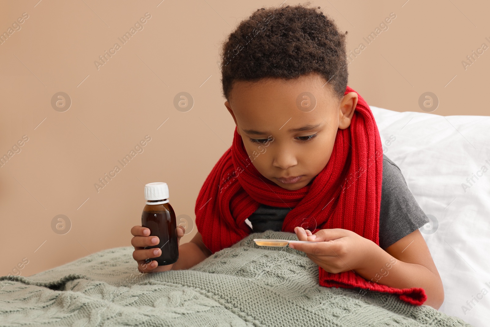 Photo of African-American boy taking cough syrup on bed at home. Cold medicine