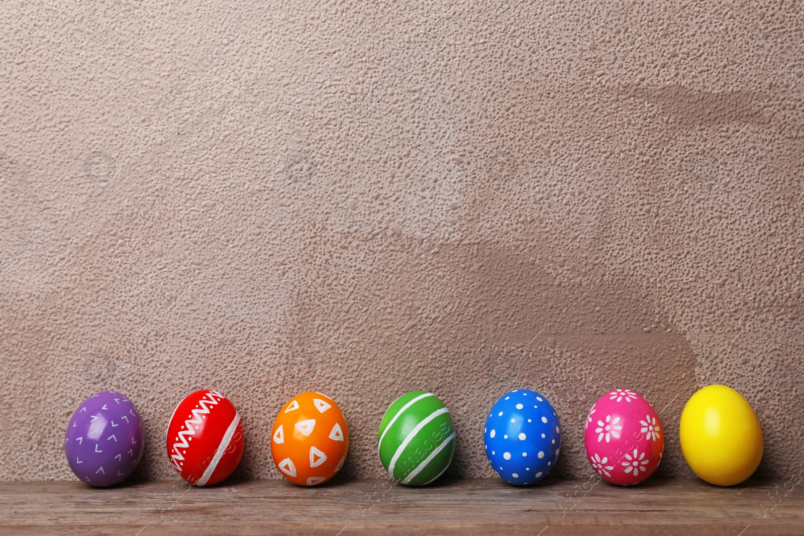 Photo of Decorated Easter eggs on table near color wall. Space for text