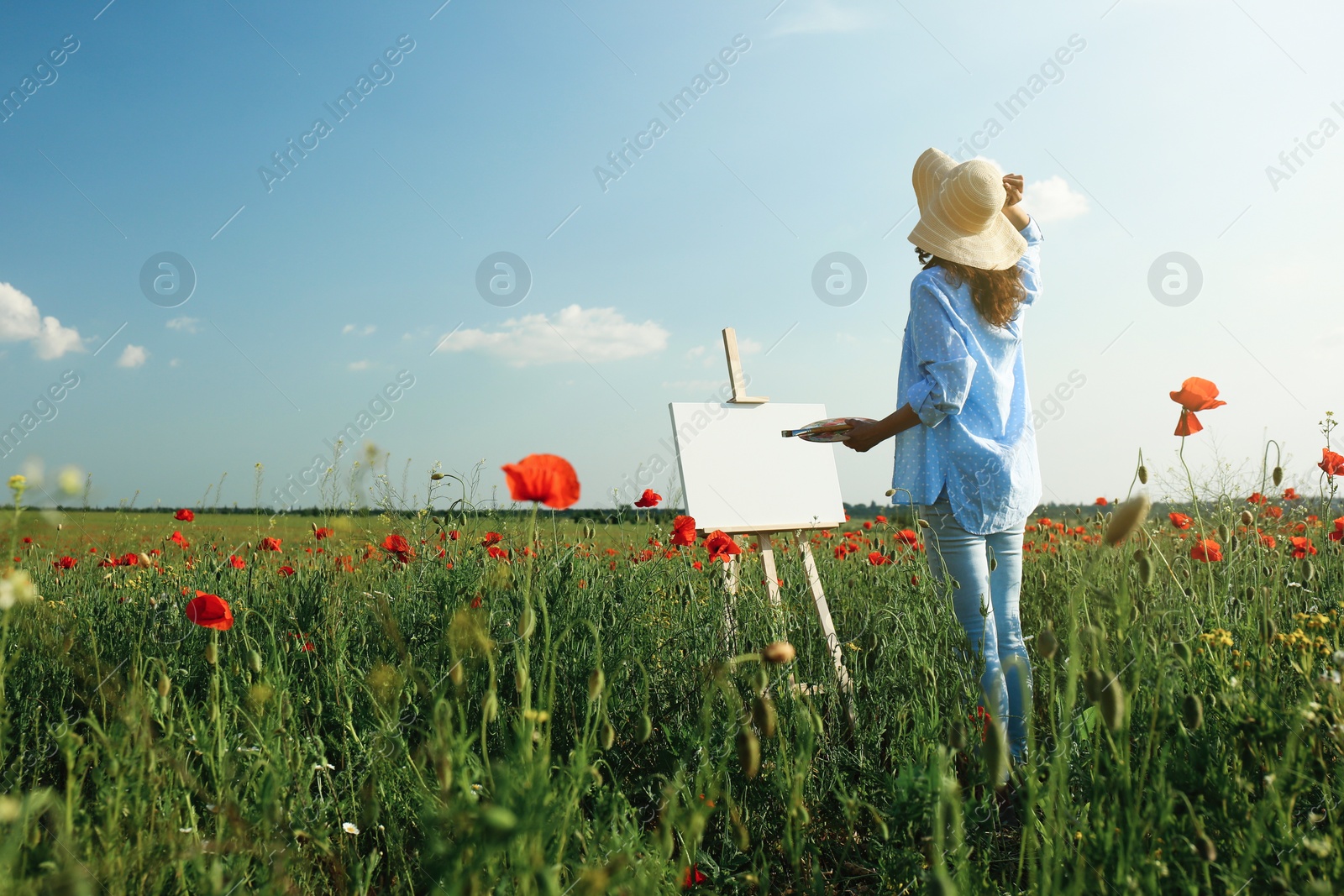 Photo of Woman painting on easel in beautiful poppy field