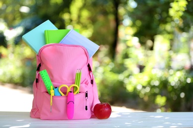 Backpack with school stationery on table outdoors