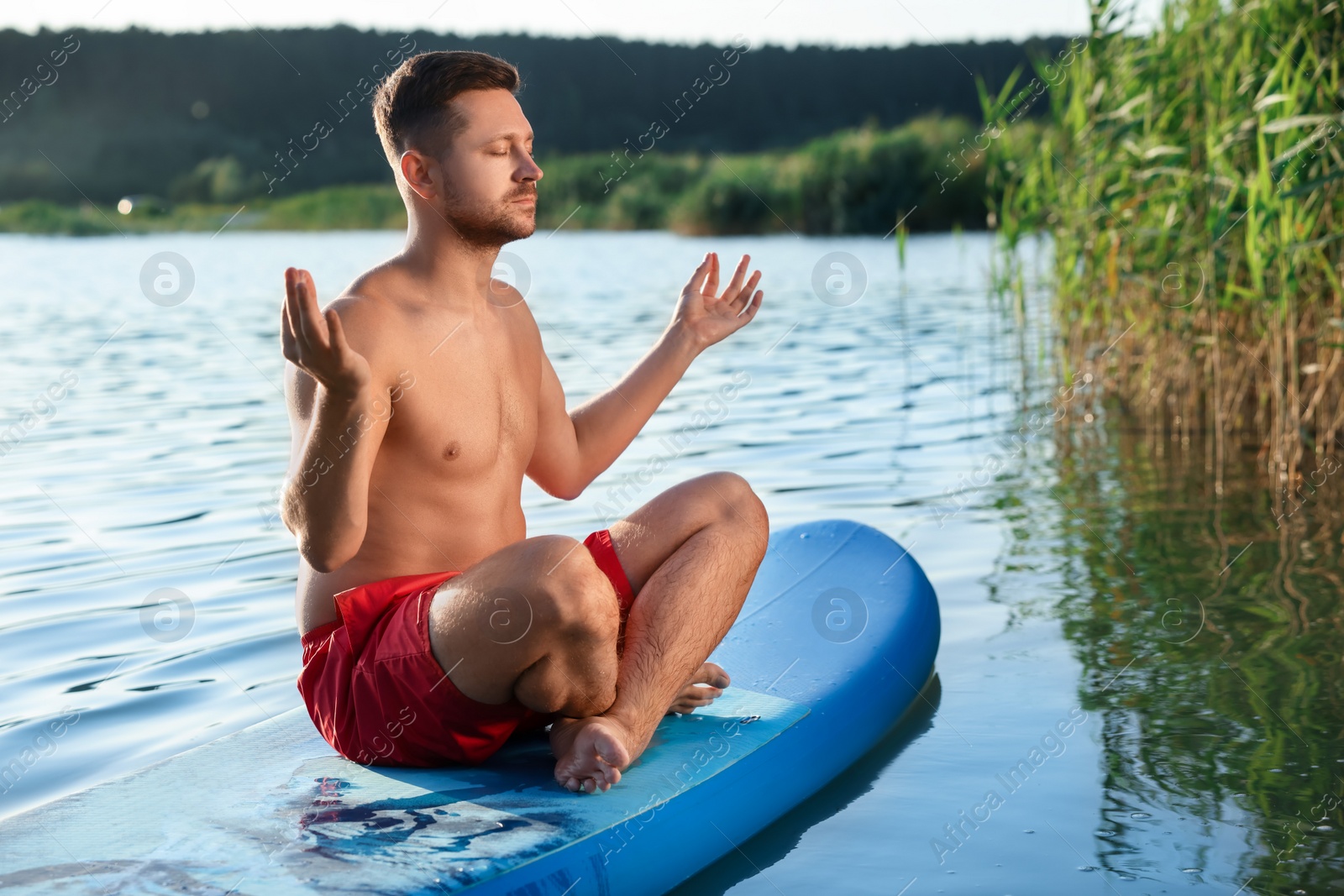 Photo of Man meditating on light blue SUP board on river at sunset