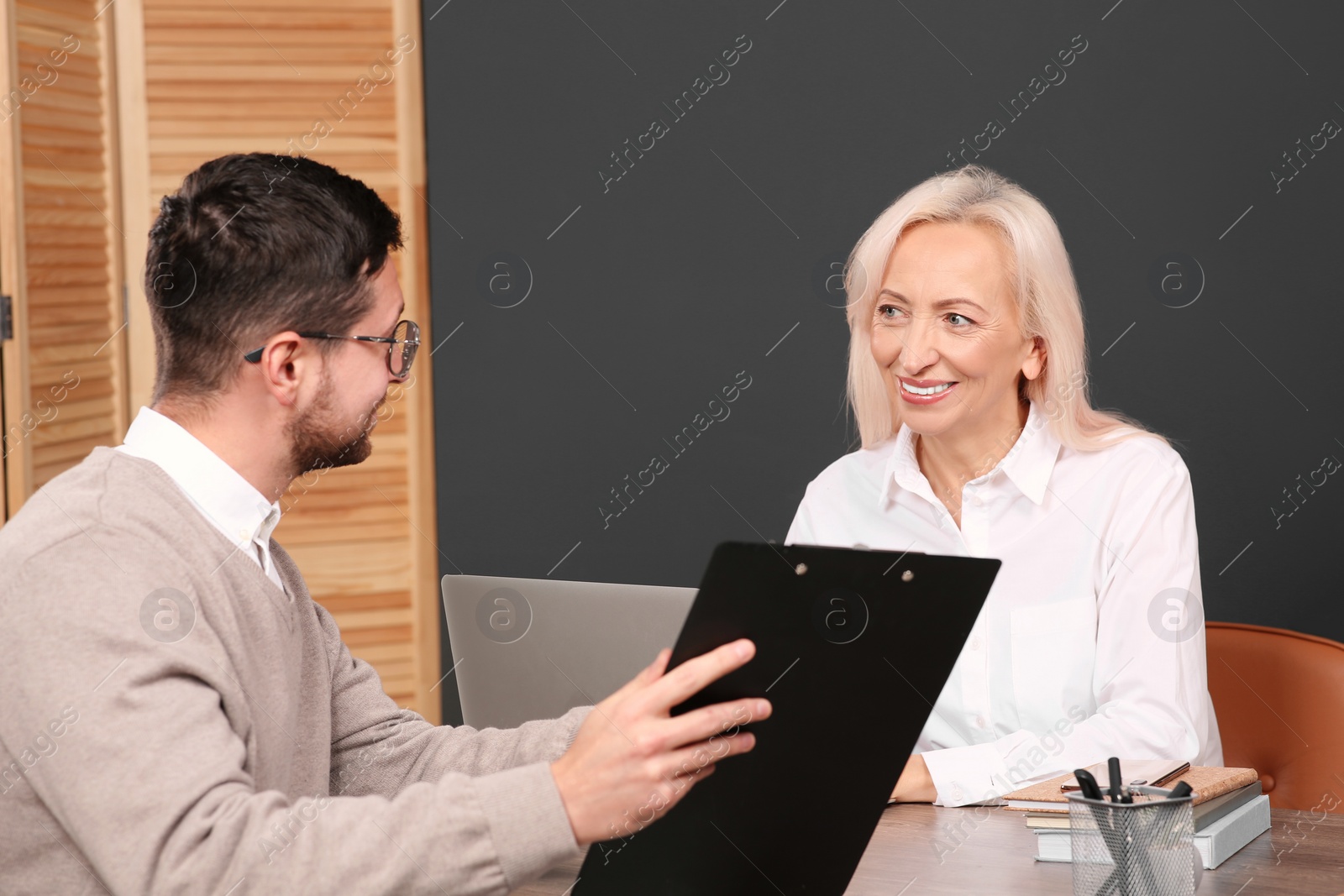 Photo of Man with clipboard and woman at wooden table in office. Manager conducting job interview with applicant