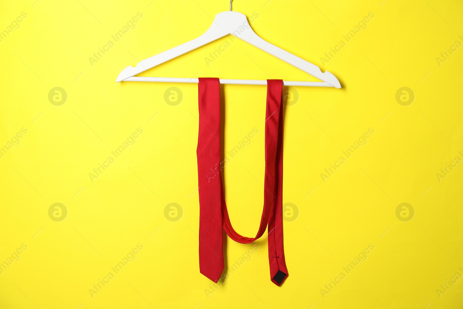 Photo of Hanger with red necktie on yellow background