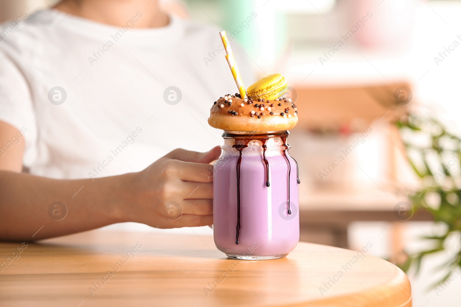 Photo of Woman with mason jar of delicious milk shake at table, closeup