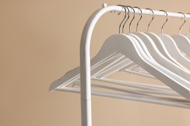 Photo of White clothes hangers on metal rack against beige background, closeup