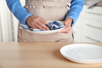 Woman wiping plates with towel in kitchen, closeup