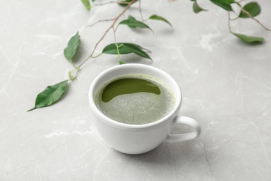 Cup of matcha tea and leaves on light background