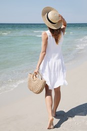 Woman with beach bag and straw hat near sea, back view